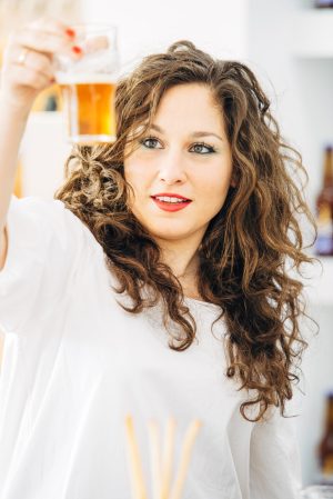 Portrait of beautiful smiling woman looking at glass of light craft beer